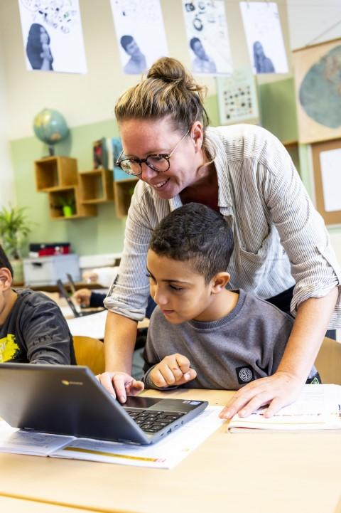Een leraar van De Kleine Wereld wijst een leerling de weg op de laptop